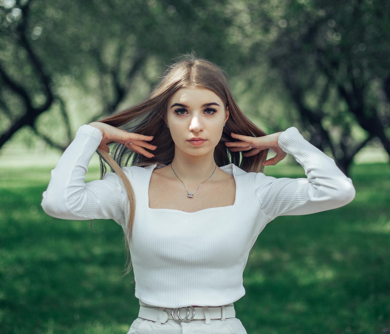 Young woman in white top standing in a green park setting.