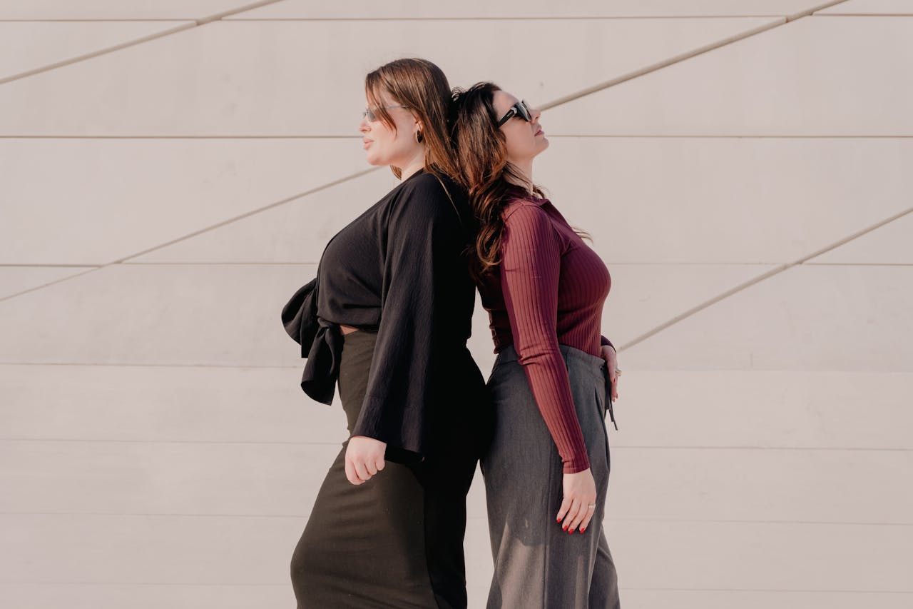 Two fashionable women standing back to back against a modern wall, showcasing contrast and style.